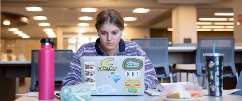 Centre student studying on laptop inside the library at table with water bottle next to her