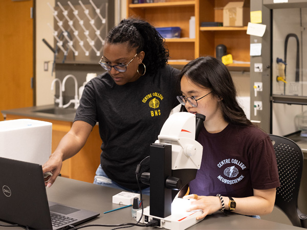 Faculty working with student in lab with a microscope