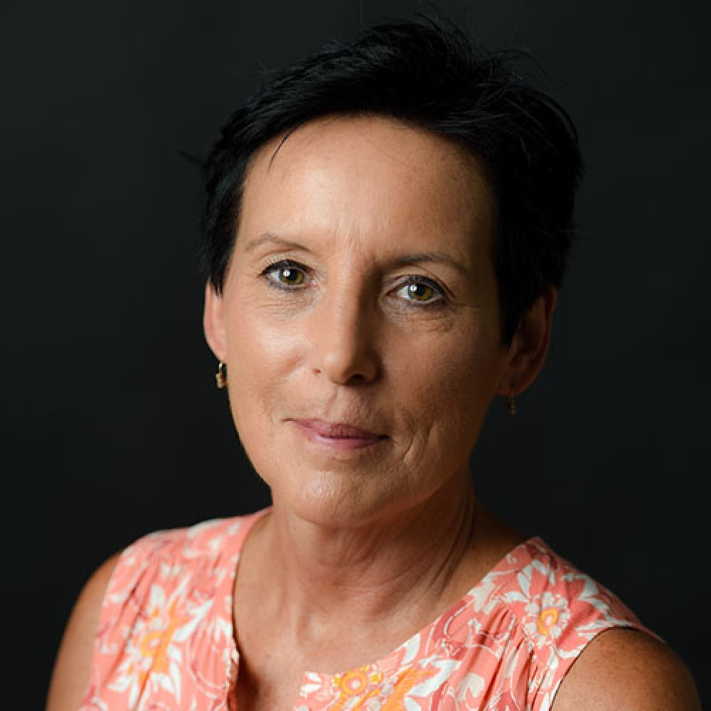 Lady with dark hair and pink paisley top in front of black background