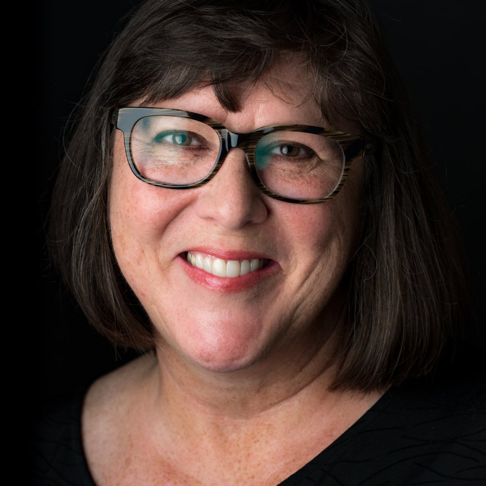 Lady with dark hair wearing glasses and black top in front of black background