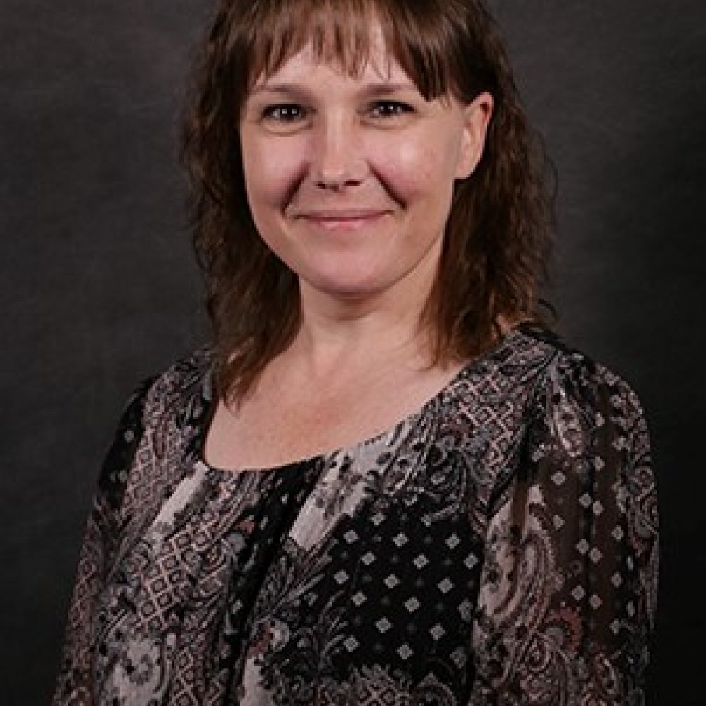 Lady with dark brunette hair wearing black and white paisley top in front of dark background