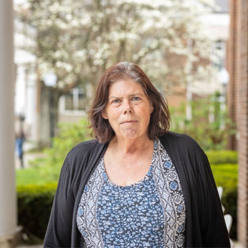 Lady with dark hair wearing multi patterned top and black cardigan standing on porch