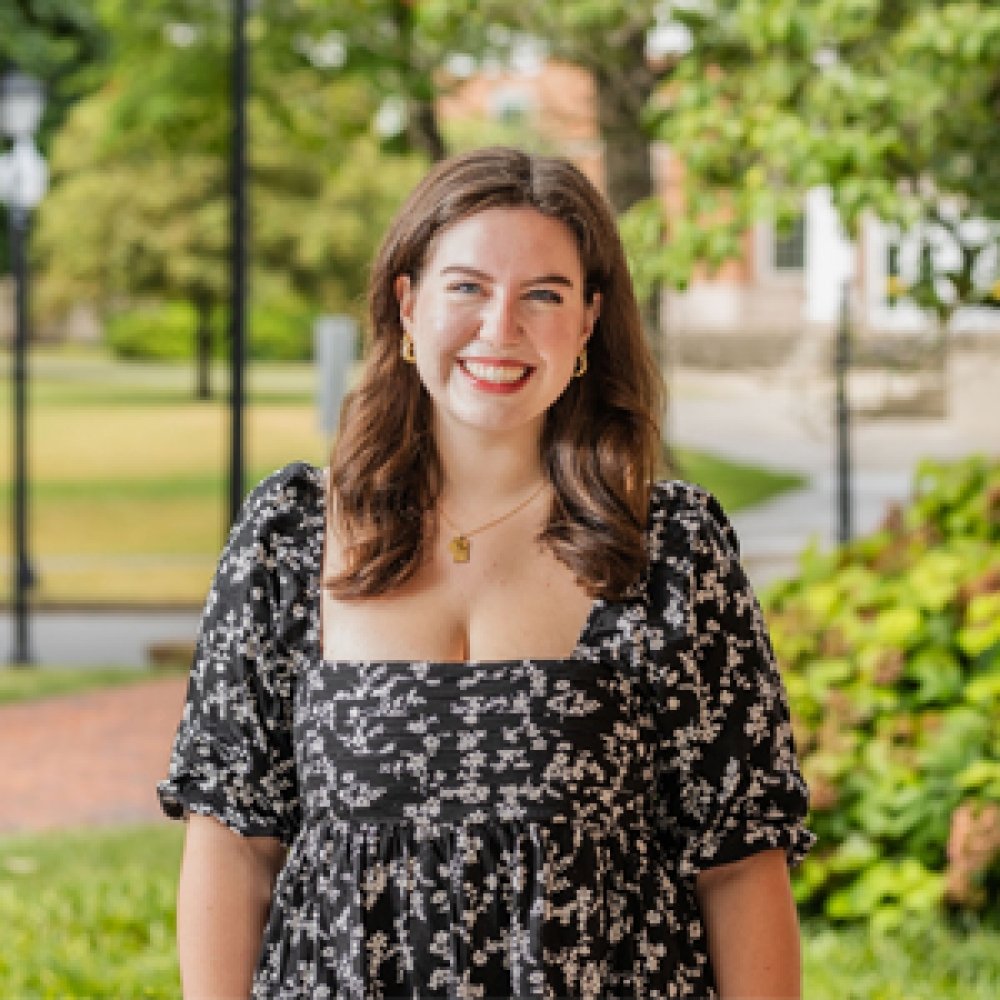 Lady with shoulder length brunette hair wearing black and white floral dress standing outside on campus