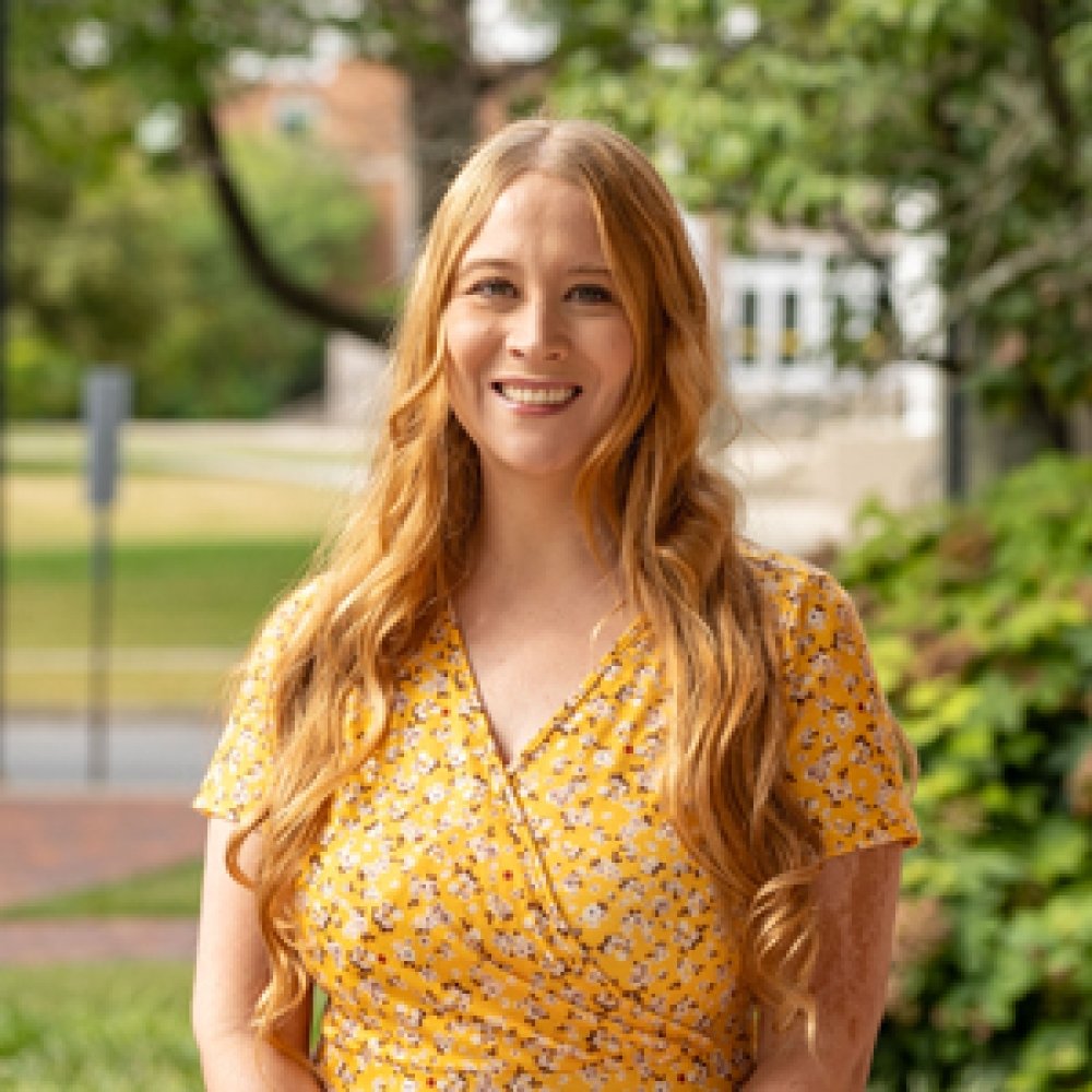 Lady with blonde hair wearing yellow floral dress outside on campus