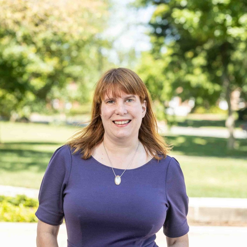 Lady with blue dress with necklace standing outside on campus