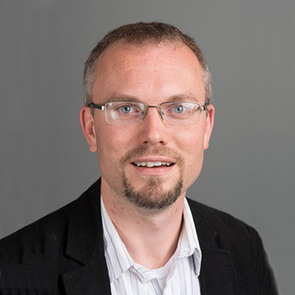 Person wearing glasses and suit jacket and blazer and smiling