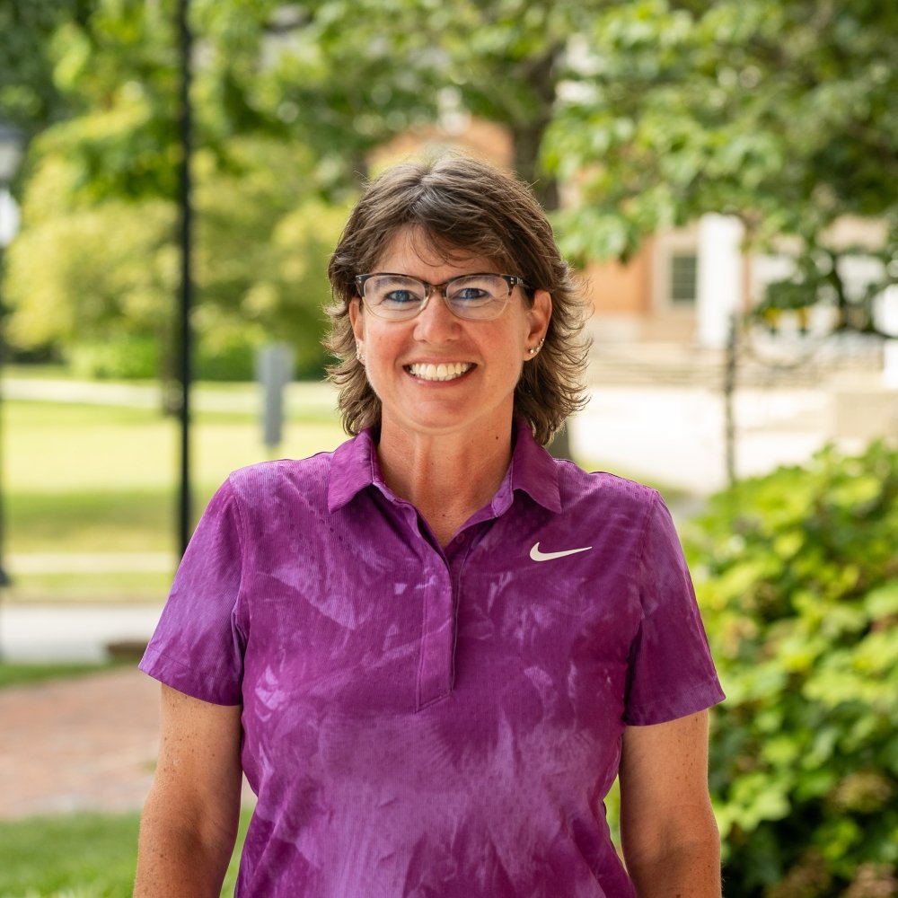 Person wearing purple polo shirt and glasses and smiling at camera