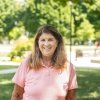 Lady with shoulder length dark hair wearing peach polo shirt standing outside