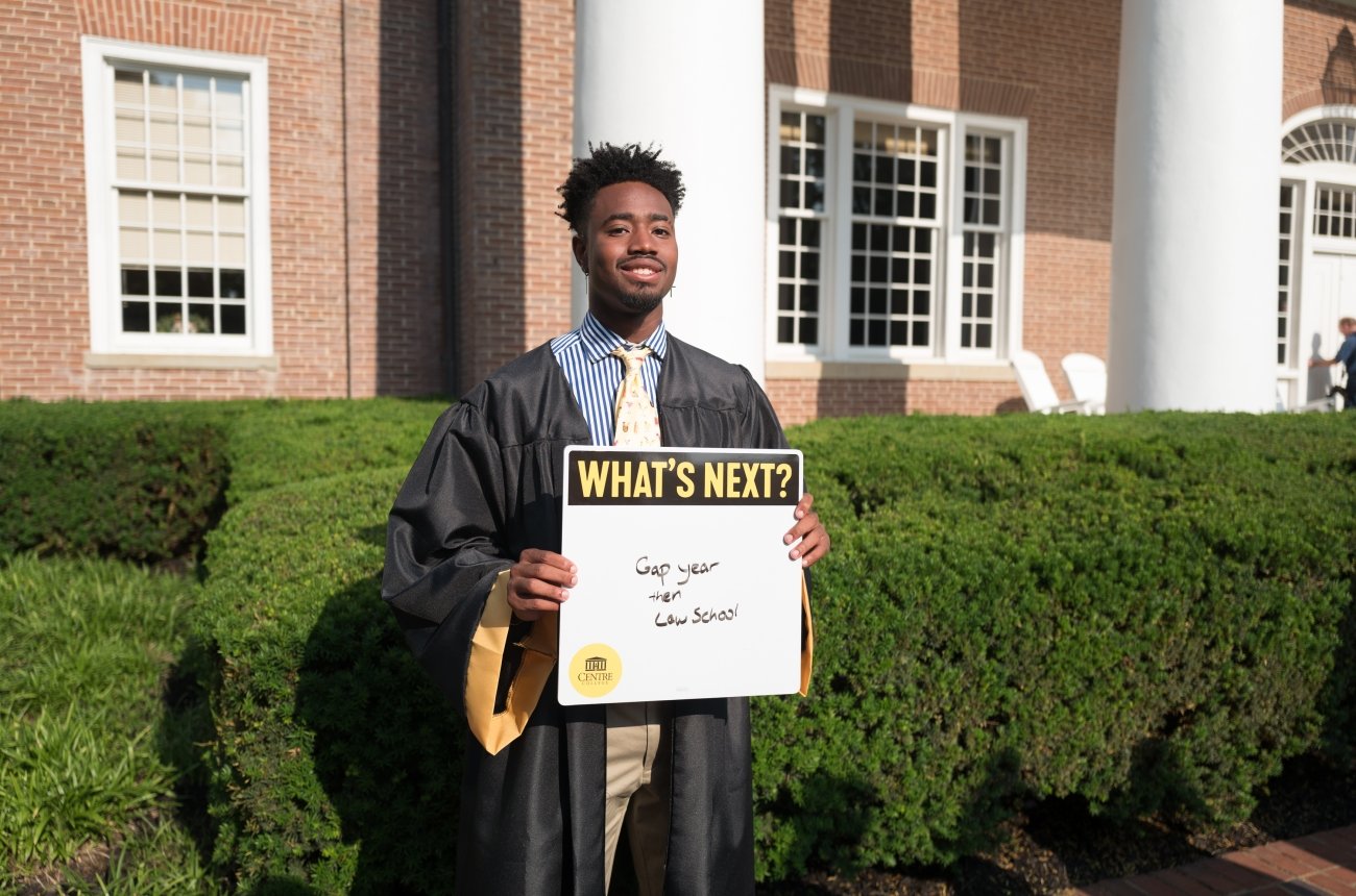 A graduating student holds a sign that reads "What's next? Gap year and then law school"