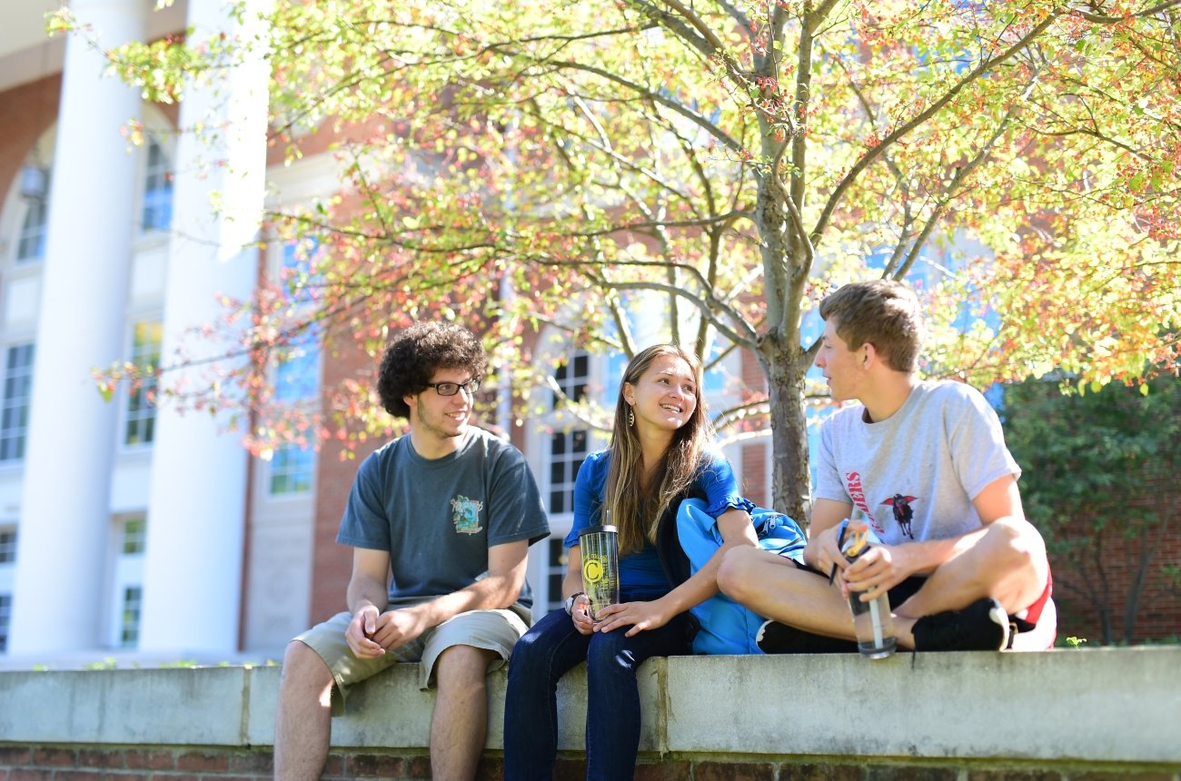 Three students sit on a wall, talking