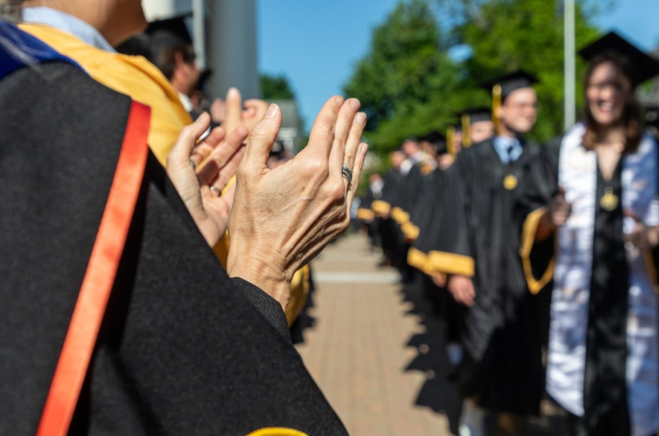 Group of faculty cheering for students as they walk by on graduation