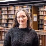 Person standing inside library and smiling at photographer