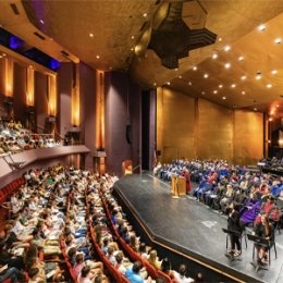 Crowd in seats and faculty sitting on stage of the Norton Center for the arts