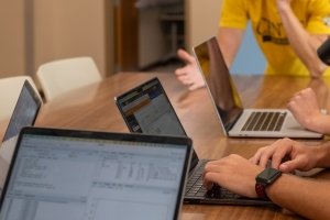 Open laptop computers are seen on a table with hands working on the keyboards.