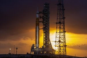 The Artemis II rocket is seen on the launch pad prior to blasting off into space with the sun setting behind it.