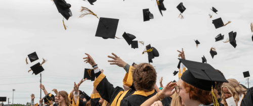 A close up of graduates throwing their caps into the air at the end of the ceremony.