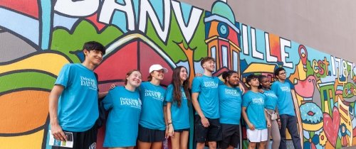 Nine students wearing identical t-shirts pose in front of a colorful mural that says "Danville."
