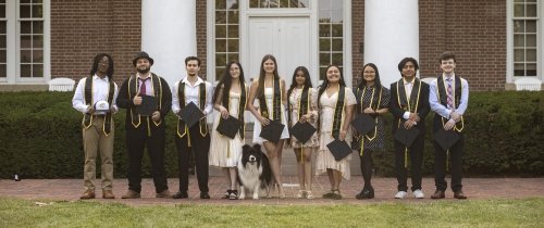 Group of students holding their graduation caps and wearing stoles on top of their dress clothes