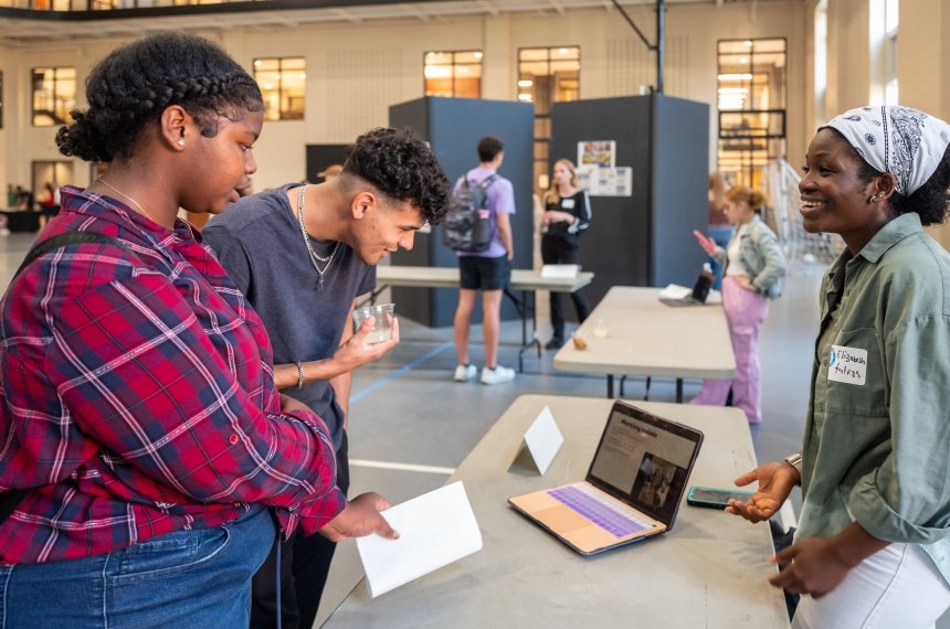 A young man and woman look at a laptop computer while a woman on the other side of the table tells them about her internship.