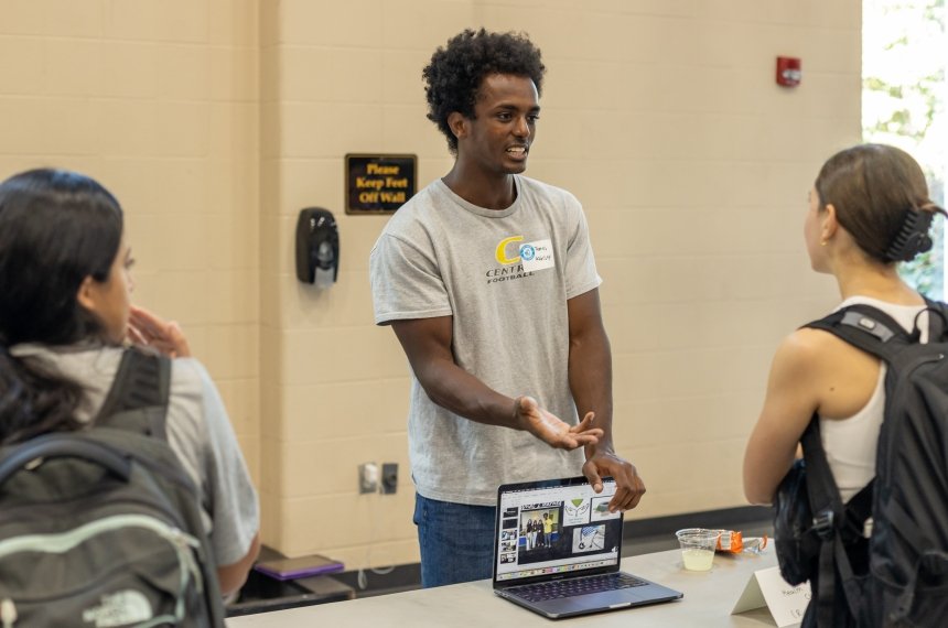A young man shows two women photos on a laptop computer.