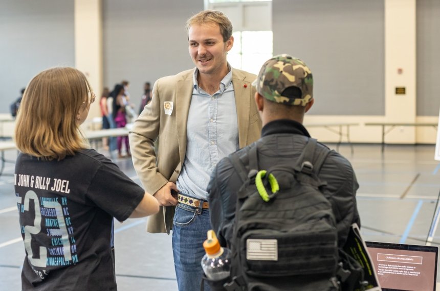 Two young women stand with their backs to the camera while talking with a man.