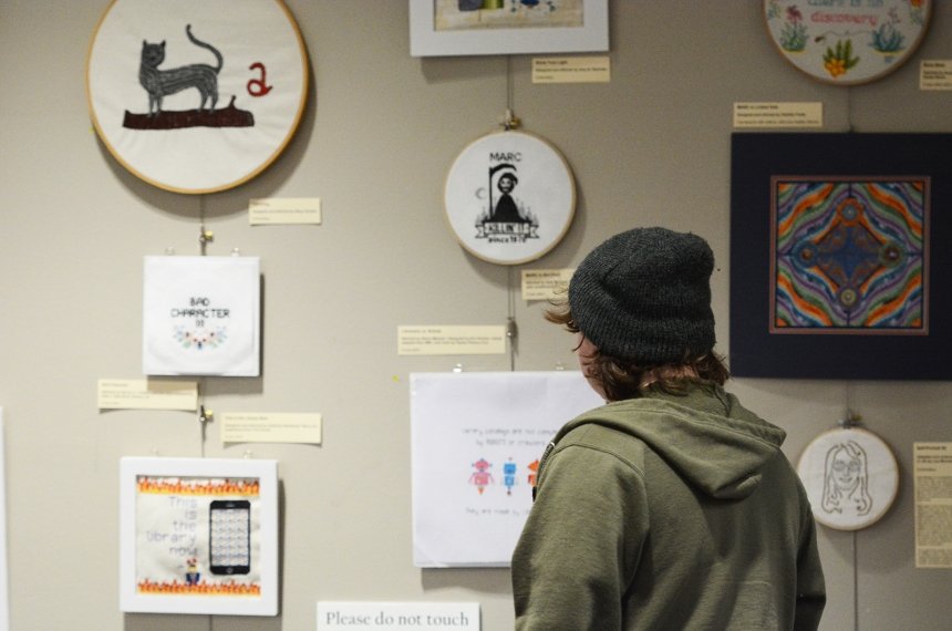 A student looks at textile art displayed on a wall.