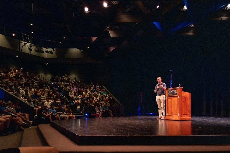 A man looks into the audience while speaking from a stage. 