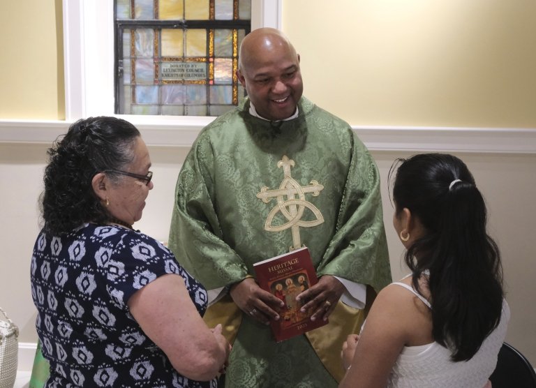 A priest wearing green and gold robes speaks with a young girl and a woman following the conclusion of a service. 