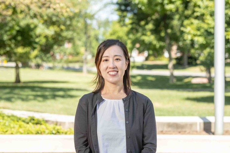 Lady with shoulder length hair wearing black cardigan and white blouse standing outside on campus