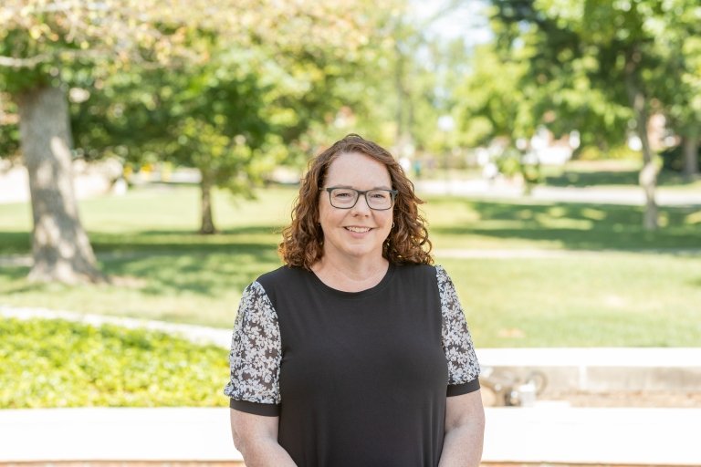 Lady with short curly hair wearing black blouse standing outside on campus