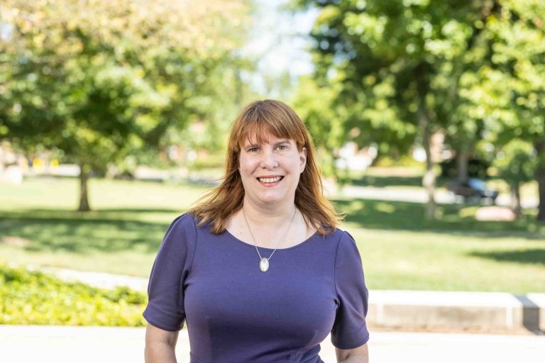 Lady with blue dress with necklace standing outside on campus