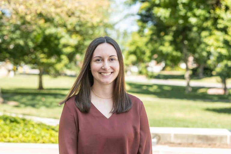 Lady with dark hair wearing maroon blouse standing outside on campus