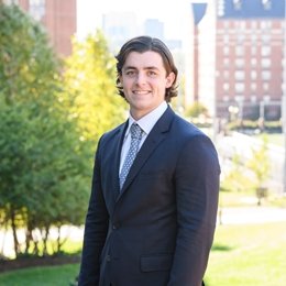 Person smiling while wearing suit standing outside