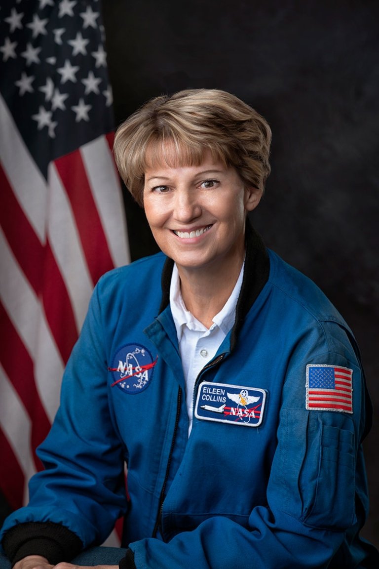 A woman wearing a NASA jumpsuit poses for a photo in front of an American flag. 