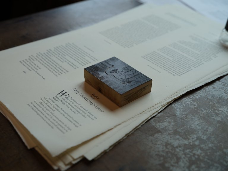An ink-covered printing block is seen atop sheets of paper covered in type. 