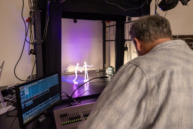 A man makes adjustments to a control panel as two posable miniature figures are seen on a model stage.