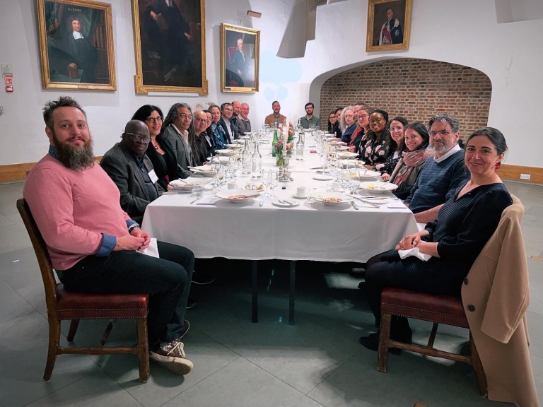 More than 15 people sit on each side of a long table covered with a white tablecloth. 