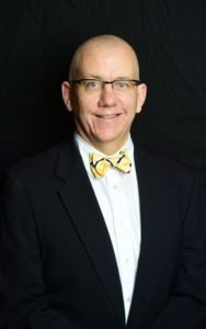 person wearing suit and yellow bow tie smiling at camera