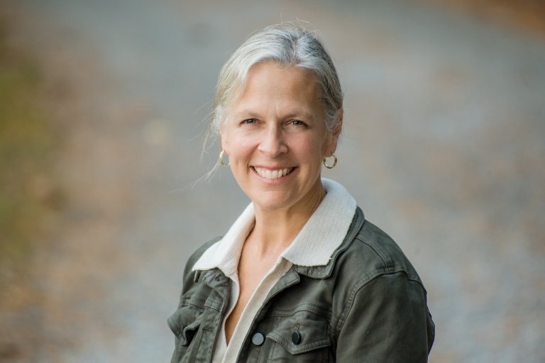 A woman wearing a collared shirt and a jacket poses for a photo outdoors. 