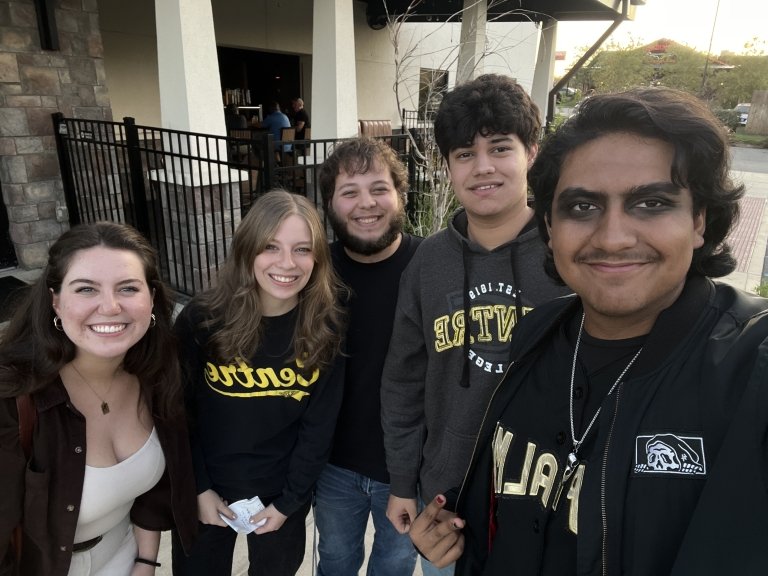 A group of students wearing Centre College shirts are outside a restaurant, smiling at the camera.