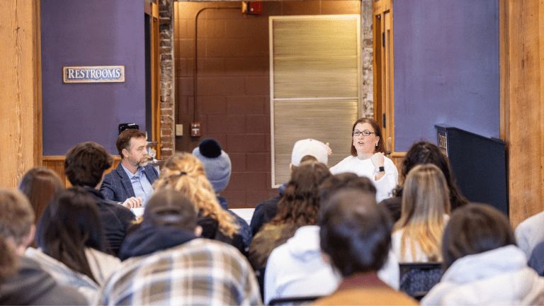 Scott Davis and a guest speaker sit in front of an attentive audience of sutdents.