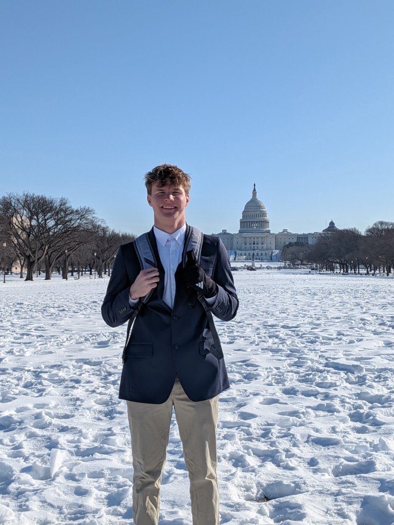 Declan Miller, wearing a backpack and suit, is on the mall in D.C. posing in front of the U.S. Capital.