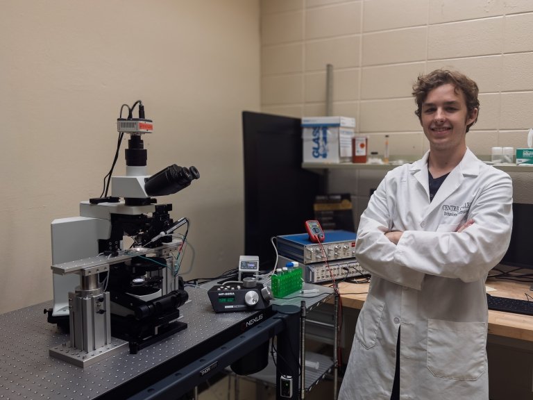Simon Forsting is standing and smiling next to his patch-clamp rig set up.
