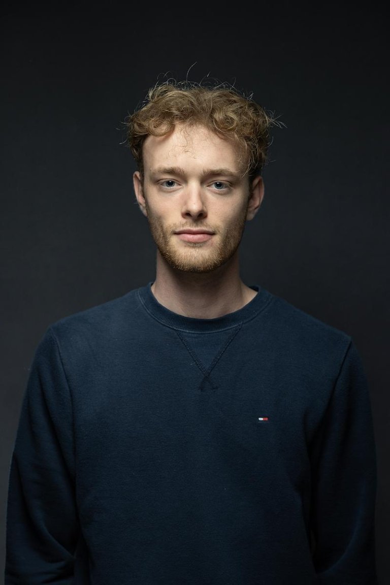 Kade Schooling posing against a dark background wearing a blue shirt.