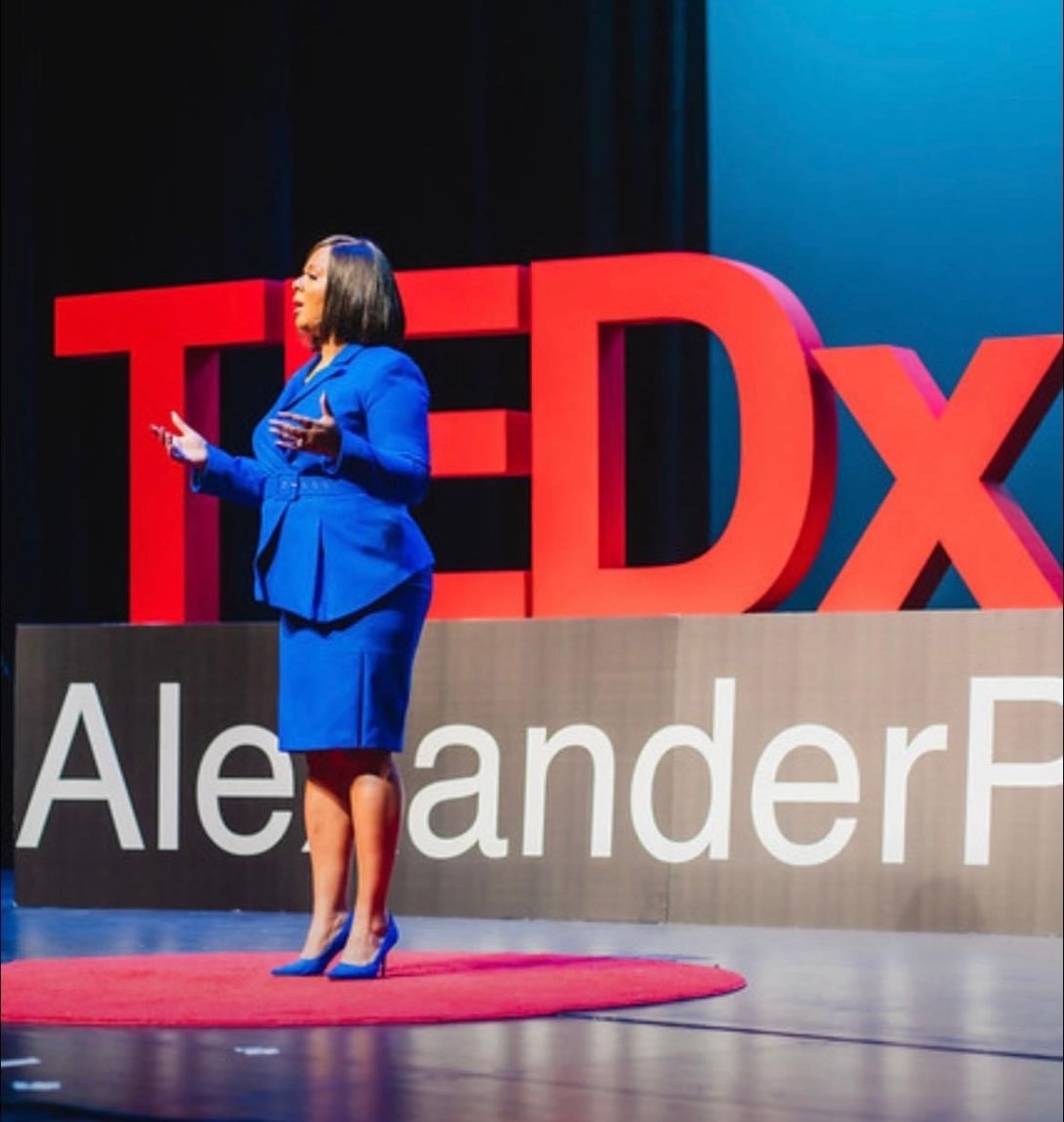 A woman speaks from a stage with the words TED x behind her. 