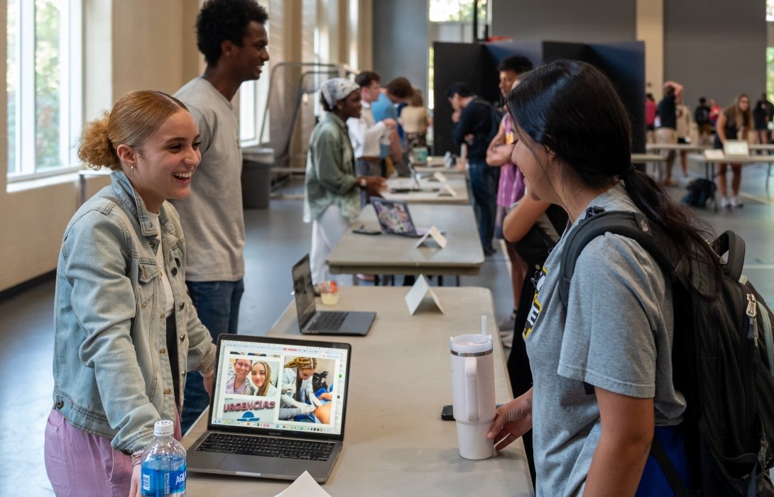 Two women talk across a table while a laptop computer shows photos of one of the women's health care internship. 