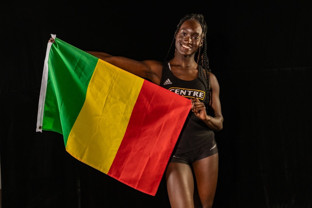 A young woman dressed in a Centre College track uniform holds the flag of Mali. 