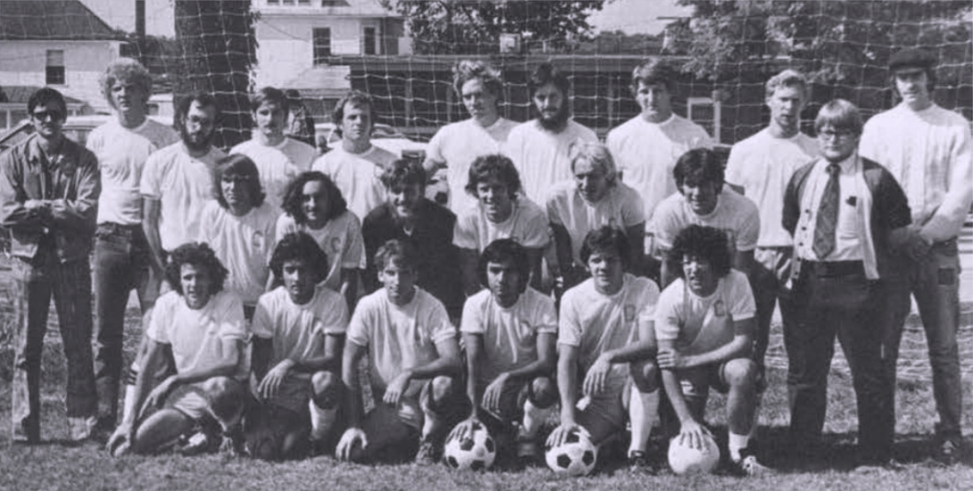 A black-and-white photo shows a soccer team posing for a photo with one row kneeling in the front and others standing behind them. 
