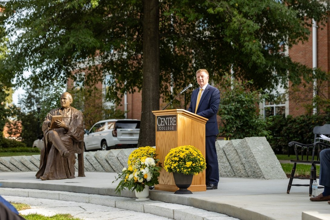 A bronze sculpture of John Marshall Harlan is seen at left while Centre president Milton C. Moreland speaks at a podium. 