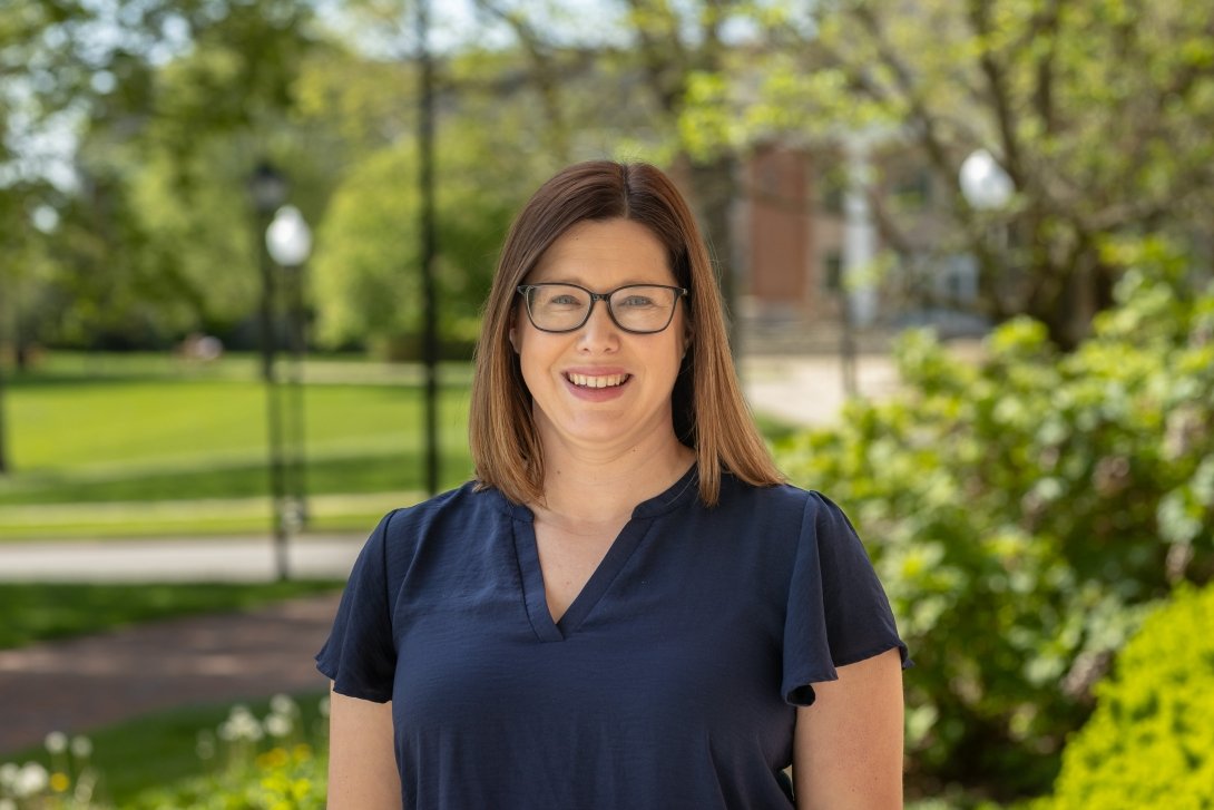 History Professor Tara Strauch poses for a photo on the Centre College campus in front of green trees and a brick building. 